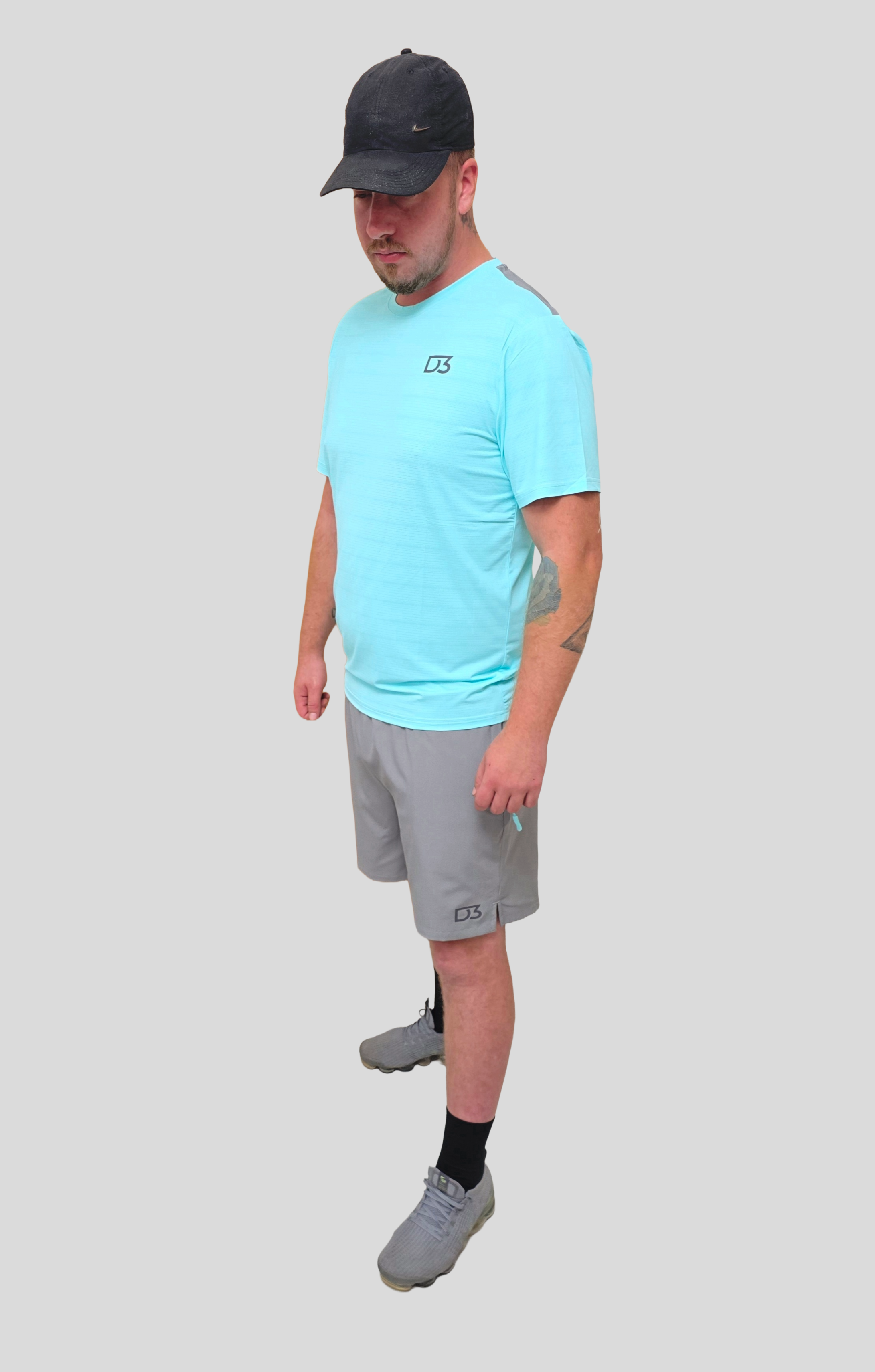 Man wearing a light blue t-shirt, gray shorts, and a black cap on a white background